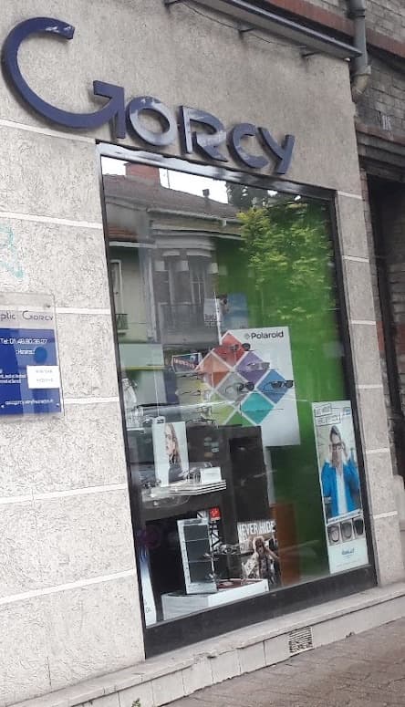 La vitrine droite de la boutique sous l’enseigne « Gorcy » en lettres bleu marine, avec la plaque des horaires